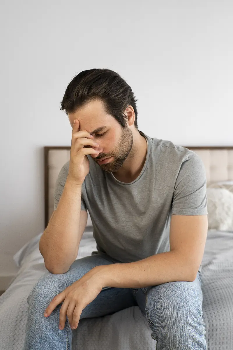 Verzweifelter Mann der auf seinem Bett sitzt.